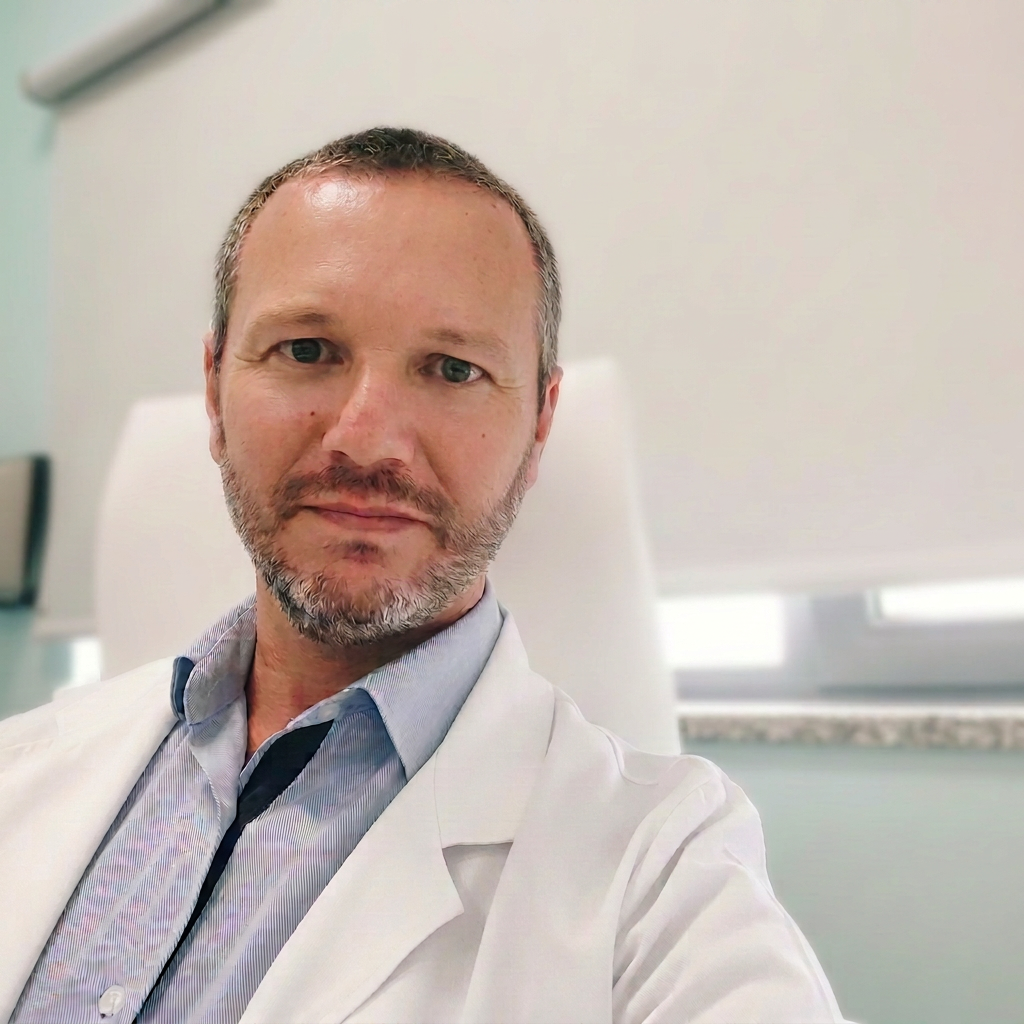 Profissional de saúde com jaleco branco, sentado em um consultório iluminado.